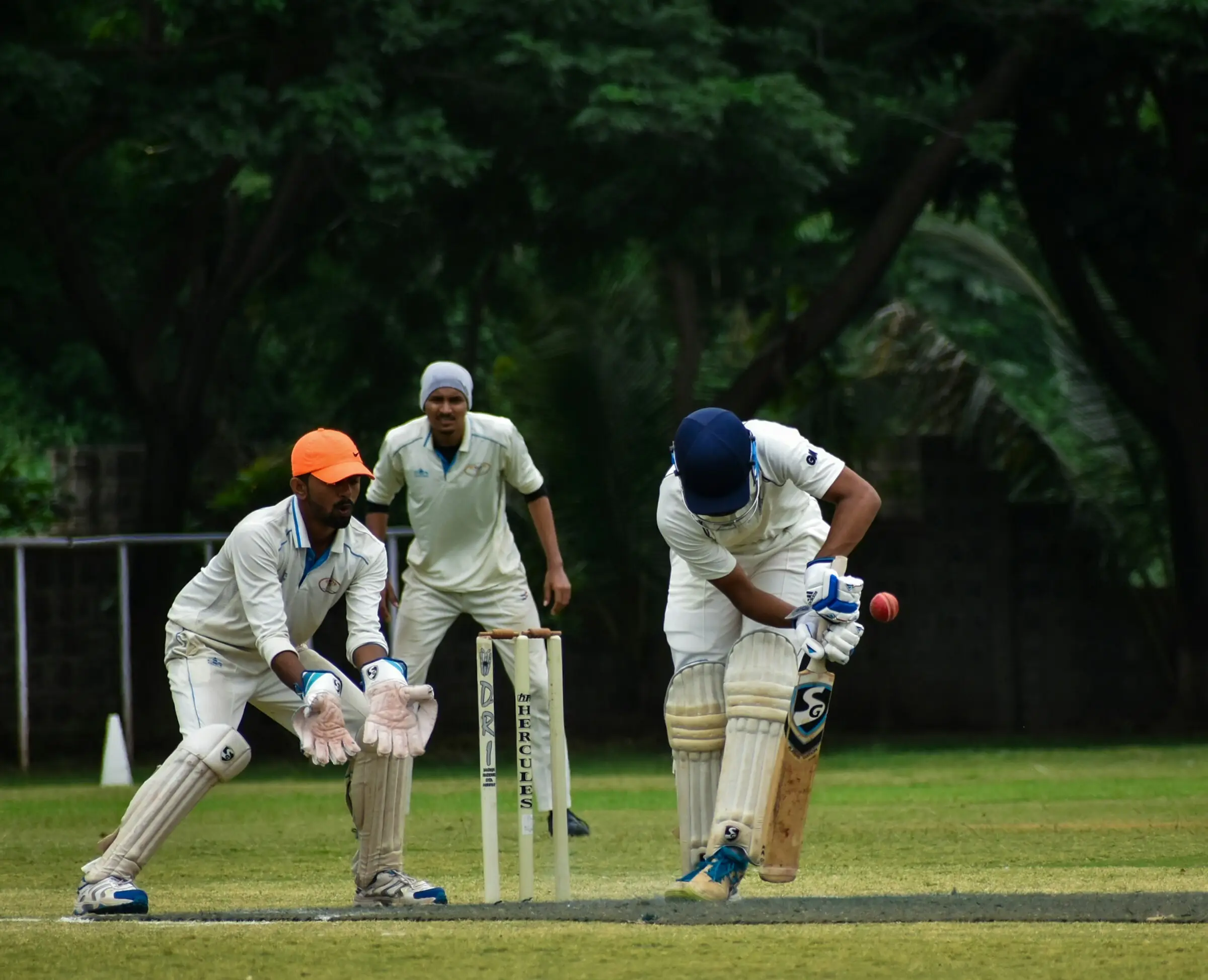 Cricket match in progress — bowler, wicketkeeper and batsman mid-play