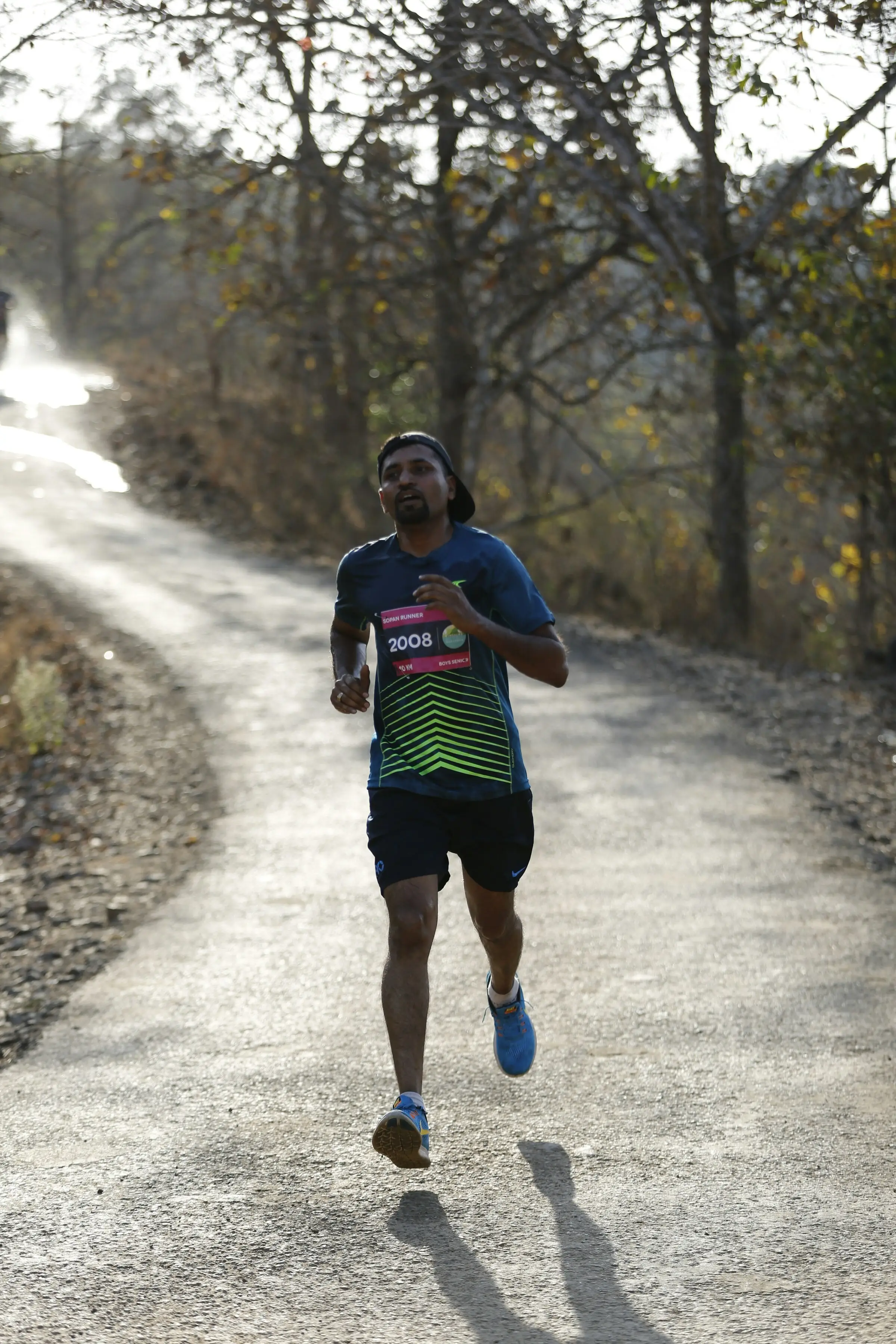Runner racing along a wooded trail, race bib on his chest